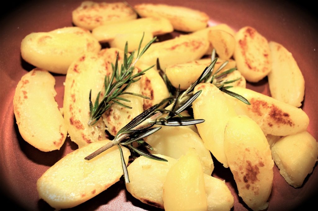 Halbierte, goldbraun gegrillte Kartoffeln mit Rosmarinzweigen auf einem Teller