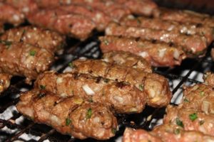 Ćevapčići mit Kräutern und Zwiebelstückchen auf einem Grillrost
