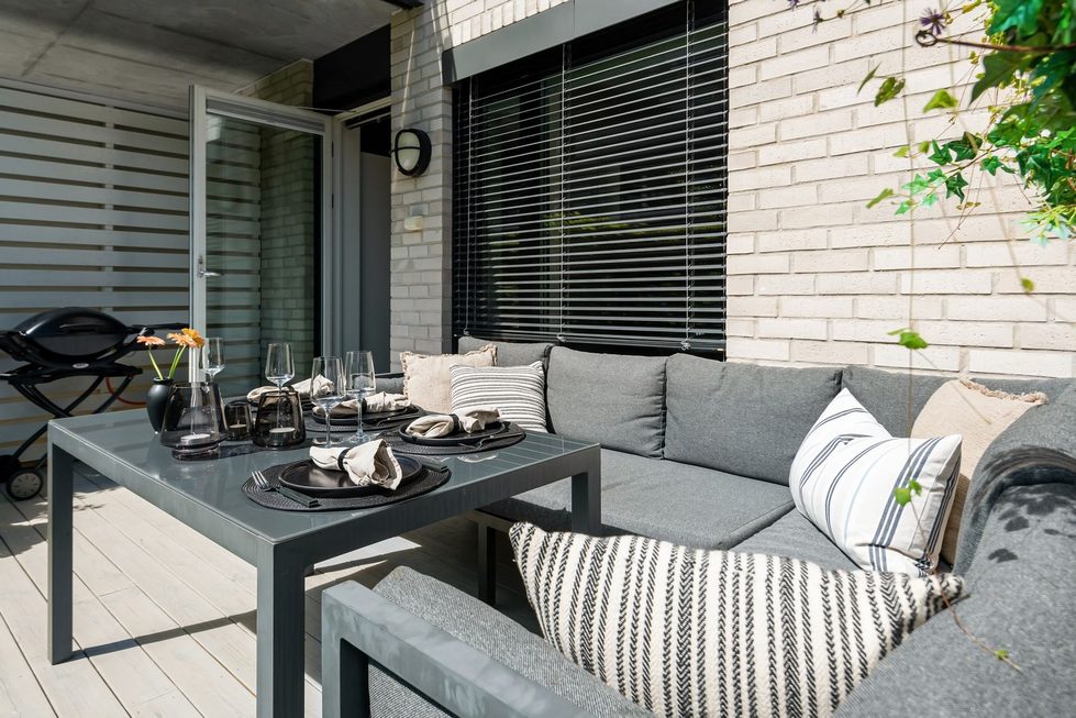 Gepflegter Balkon eines Mehrfamilienhauses mit gemütlicher Sitzecke und geschlossenem Gasgrill bei frühem Abendlicht.