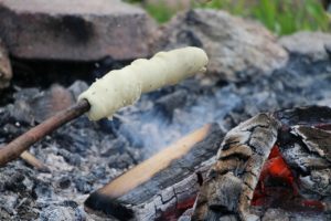 Um einen Stock gewickelter Stockbrotteig über der Glut einer Feuerstelle