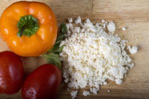 Zerbröselter Feta neben Paprika und Tomaten auf einem Holzbrett