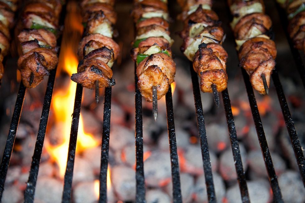 Beim feuerschale grillen liegen würzige Hähnchenspieße über glühender Kohle auf einem Grillrost, das Feuer lodert im Hintergrund.
