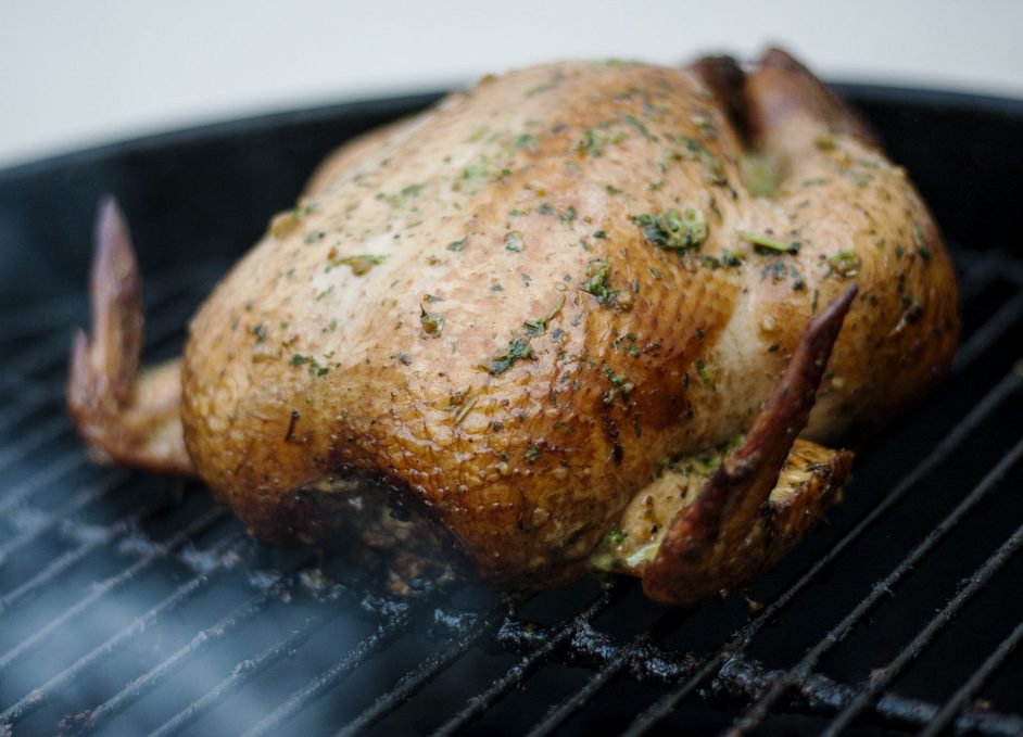 Ein ganzes goldbraun gegartes Hähnchen liegt auf dem Grillrost, daneben ist freie Grillfläche zu erkennen.