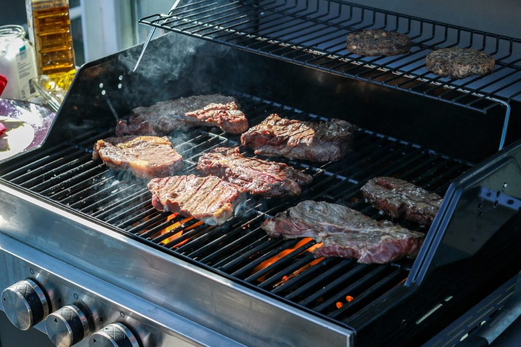 Rindersteaks auf dem Rost eines geöffneten Gasgrills mit sichtbaren Flammen