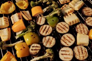 Gesund grillen im Sommer: Verschiedene bunte Gemüsestücke wie Brokkoli, Paprika und Zucchini mit Grillmuster liegen auf dem heißen Grillrost.
