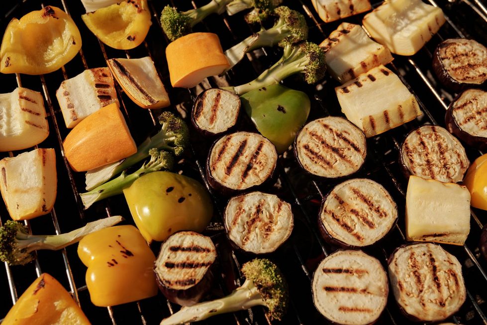 Gesund grillen im Sommer: Verschiedene bunte Gemüsestücke wie Brokkoli, Paprika und Zucchini mit Grillmuster liegen auf dem heißen Grillrost.