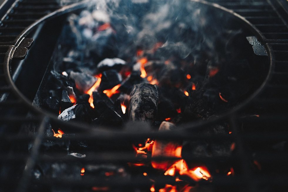 Glühende und mit Asche bedeckte Holzkohlen unter einem Grillrost bei natürlichem Licht.