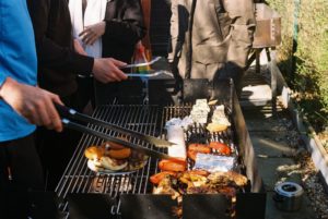 Grillen im Garten mit mehreren Erwachsenen am Grill und verschiedenen Speisen im Freien in entspannter Atmosphäre.