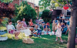 Fröhlicher Kindergeburtstag im Garten mit Grill und großzügigem Abstand zwischen Grillstation und spielenden Kindern, sicheres Grillen am Kindergeburtstag.