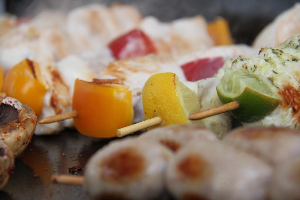 Grillspieße mit Paprika und Zitrusstücken auf einer heißen Grillplatte