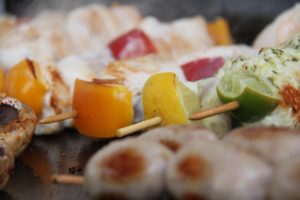 Grillspieße mit Paprika und Zitrusstücken auf einer heißen Grillplatte