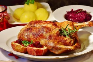 Gebratene Ente mit Apfelhälften und roten Beeren, dazu Kartoffelklöße und Rotkohl als Weihnachtsessen
