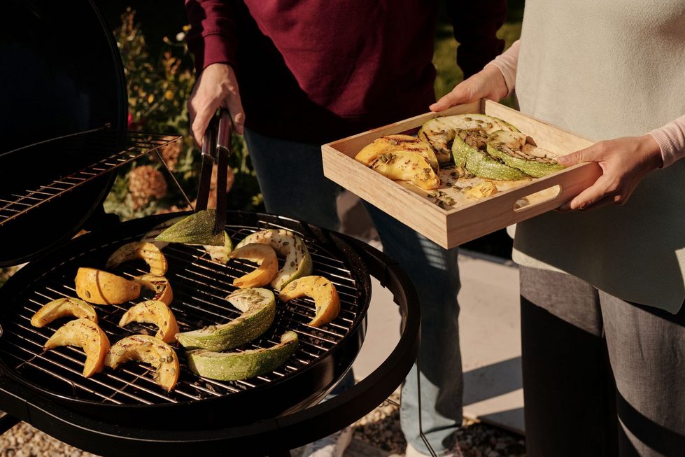 Zucchini und Kürbis werden auf einem Grill im Freien vorbereitet, während Sonnenlicht eine entspannte Gartenatmosphäre schafft.