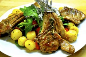 Saftig gegrillte Lammkoteletts mit Knochen und frischen Kräutern, angerichtet zu Lammlachs grillen auf einem bunten Teller mit Gemüse.