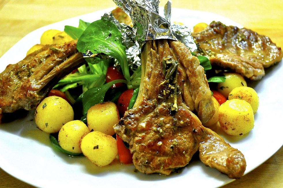 Saftig gegrillte Lammkoteletts mit Knochen und frischen Kräutern, angerichtet zu Lammlachs grillen auf einem bunten Teller mit Gemüse.
