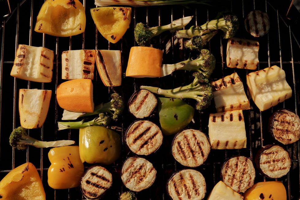 Verschiedene Sorten buntes Gemüse wie Paprika, Zucchini, Brokkoli und Aubergine werden auf einem Grill im Garten gegrillt.
