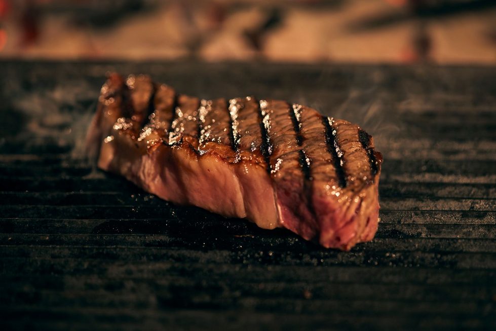 Gegrilltes Steak mit ausgeprägten Grillstreifen liegt auf dem Rost, leichter Rauch steigt auf.
