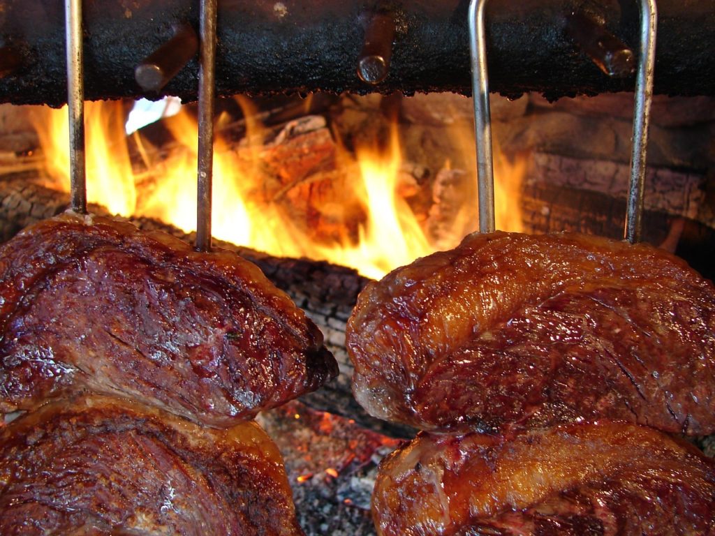 Große Rindfleischstücke an Grillspießen über offenem Holzfeuer