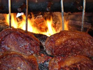 Große Rindfleischstücke an Grillspießen über offenem Holzfeuer