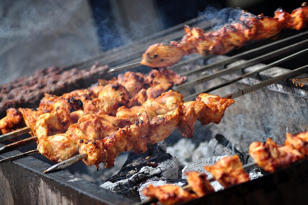 Marinierte Hähnchenspieße werden auf einem höhenverstellbaren Rost über glühender Holzkohle auf einem offenen Grill gegart.
