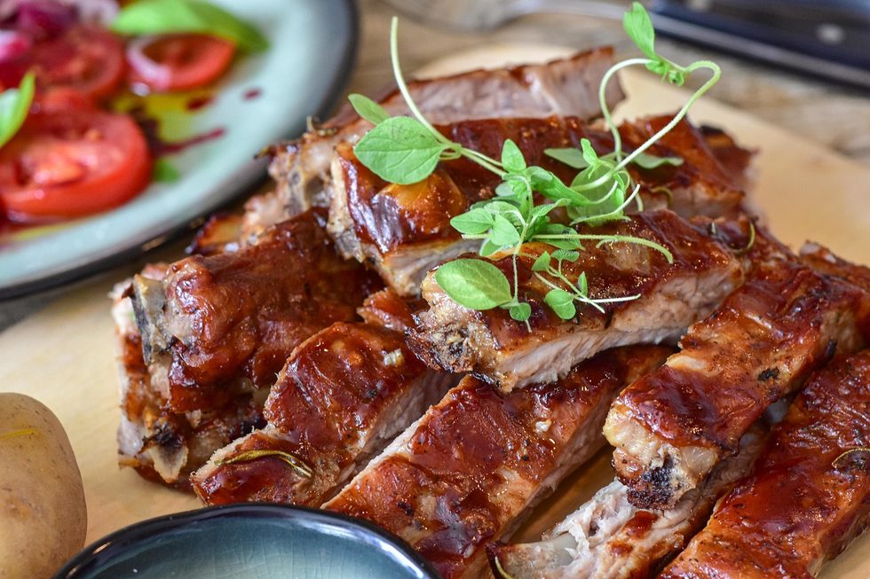 Saftige, glasierte Spare Ribs grillen auf einem Holzbrett angerichtet, garniert mit frischen Kräutern.