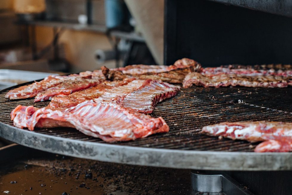 Mehrere rohe Spareribs-Leitern liegen nebeneinander mit der Knochenseite nach unten auf einem runden Grillrost, bereit für das Grillen.